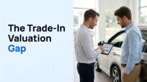 Two men reviewing a trade-in valuation on a tablet beside a car in a dealership showroom, with the title "The Trade-In Valuation Gap"