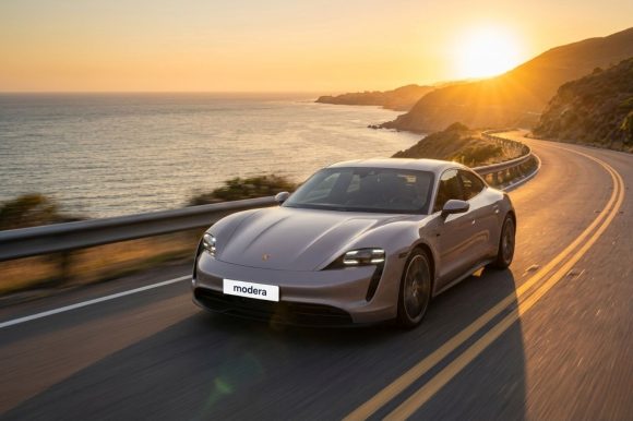 Silver car driving on a coastal road at sunset with Modera branding on the license plate